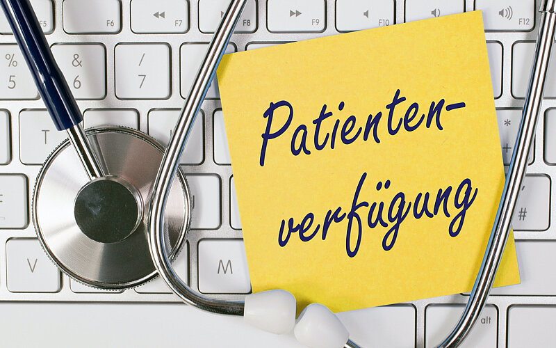 Das Wort "Patientenverfügung" steht auf einem Post-It Zettel, der auf einer Tastatur liegt.